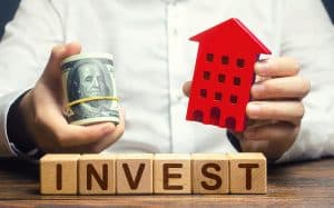 A Man With Dollars And A House Figurine And The Word Invest. 